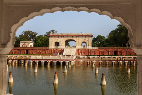 View of a serene water garden with symmetrical rows of white-tipped pillars reflecting against the red brickwork, captured through a white archway, Lahore, Punjab, Pakistan.