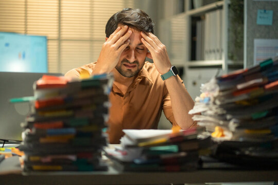 Hispanic accountant in crisis mode, battling worries about bankruptcy and financial issues while working overtime in a cluttered and stressful office environment.
