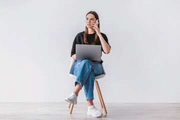 Troubled young woman with laptop sitting on chair, making phone call, having problem with online...