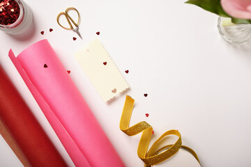 Gift wrapping supplies with gold ribbon, pink and red paper, scissors, red hearts. Valentine's Day or Mother's Day background.