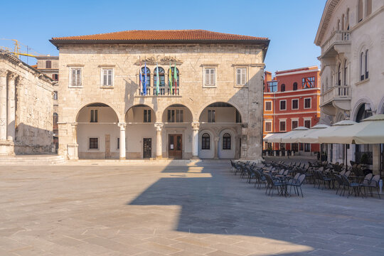 View of the sun-drenched Forum Square reveals ancient architecture, with stone buildings casting long shadows, a vivid tableau of history and light, Pula, Istria County, Croatia.