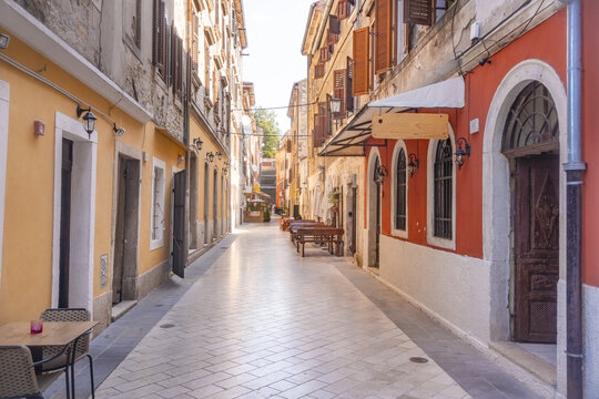 View of sunlit street lined with buildings painted in warm hues of yellow and red, casting shadows on the bright pavement, Pula, Istria County, Croatia.