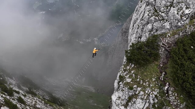 Aerial view of a man crossing a suspension ladder between mountains