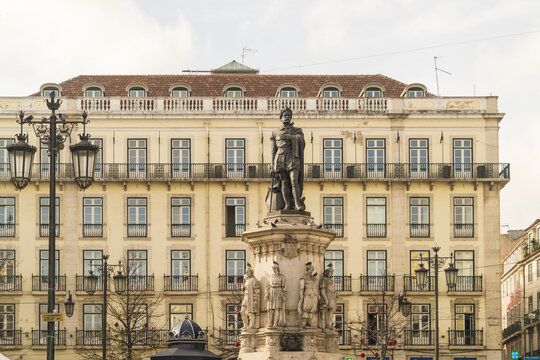 View of a statue standing tall on a plinth surrounded by ornate streetlights and a neoclassical building with rows of windows, Lisbon, Lisbon, Portugal.