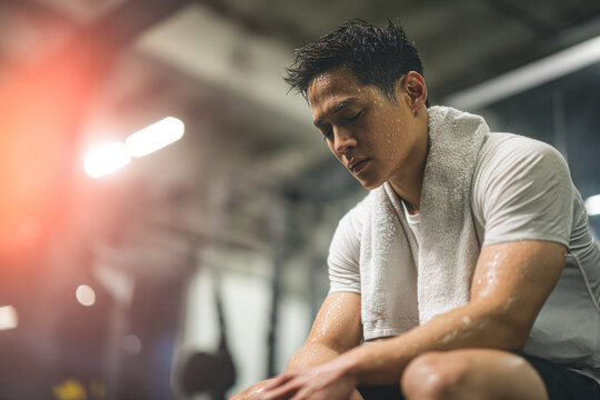A focused athlete resting after a workout, showcasing determination and effort, with sweat glistening on his skin in a gym setting.
