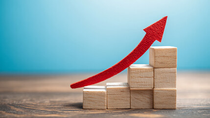 Wooden blocks stacked in ascending order with a red arrow indicating growth and success on a wooden surface with a blue background