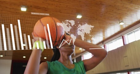 Raising orange basketball overhead, player wearing green tank top, neon wristband with HUD in gym