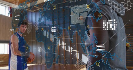 Pointing at data overlay, hooded coach guiding player in jersey holding basketball on court