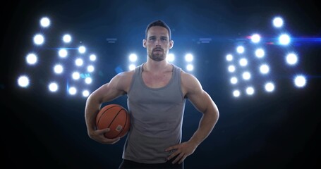 Holding orange basketball, male athlete posing at gym with gray tank, LED panels, lens flare © vectorfusionart