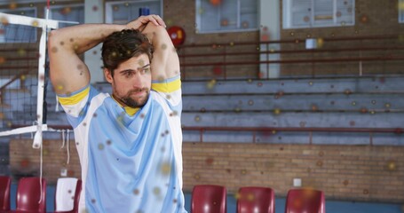 Stretching athlete in blue jersey extending triceps in gym by net post, bleachers, copy space