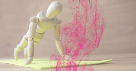 Balancing wooden mannequin doing diagonal crawl pose on yellow pad on table, with pink powder plume