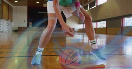 Bending adult female basketball player wearing white shorts on gym floor, basketball rolling