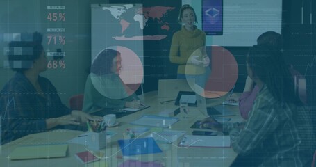 Leading presenter in yellow sweater gesturing and explaining wall display charts in meeting room