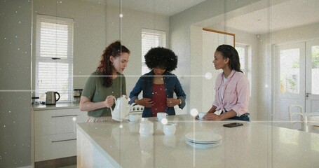 Obraz premium Pouring tea, three women in green-tee, denim-jacket, pink-top talking in modern kitchen with teapot
