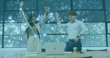 Raising arms, two coworkers cheering behind table in business attire with open laptop and overlay