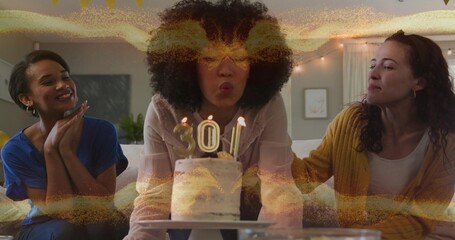 Leaning center woman wearing light blouse blowing out number 30 candles on birthday cake at home