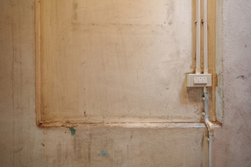 A close-up view of a weathered beige concrete wall featuring a white three-button light switch connected to vertical electrical conduit pipes.