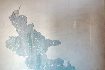 A close-up texture view of a damaged wall surface where layers of beige paint are peeling and chipping away to expose a scratched turquoise blue concrete background.