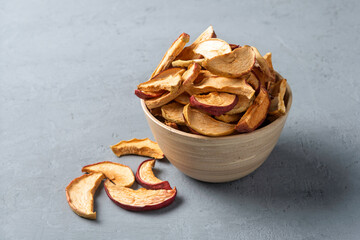 Wood bowl holds dried apple slices on gray table, clean simple copy space for healthy snack, hiking food, vegan diet branding.
