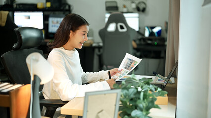 Female graphic designer working on logo creation with drawing tablet and color palette in modern bright office.