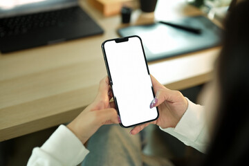 Hands holding smartphone with blank white screen in home workspace for mockup use