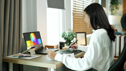 Female graphic designer working on logo creation with drawing tablet and color palette in modern bright office.