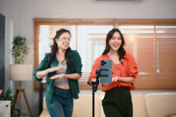 Two girl dancing and making videos filming vlog with online content focus with smartphone