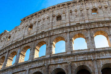 Obraz premium Famous Coliseum in Rome. Colosseum, or Coliseum. Part of the wall of an antique stone structure with arches. Italy, Europe. Famous touristic place in the world, Europe. Beautiful blue sky background.