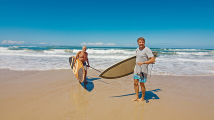 Young and elderly surfers walk with surfing boards on the beach in Brazil