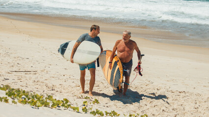 Young and elderly surfers walk with surfing boards on the beach in Brazil