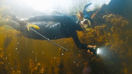 Woman with speargun swims in the lake with freshwater weed
