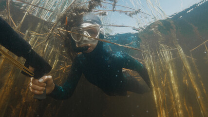 Woman with speargun swims in the lake with freshwater weed