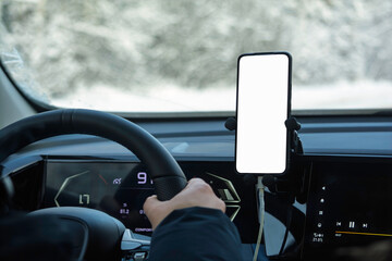 Driver hand on steering wheel with smartphone on dashboard mount and blank screen, winter road view, modern car interior mockup