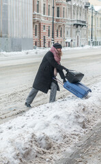 A young woman with a suitcase and bags struggles through snowdrifts onto the road. Collapse in the city. Selective focus