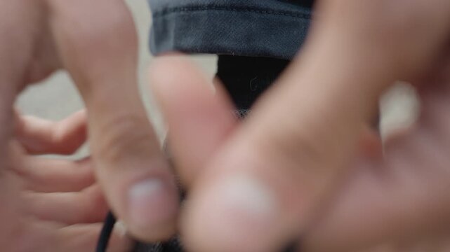 Closeup mans hands tying sneaker lace into secure bow, focused fingers pulling aglet and looping tight, jeans cuff and sock visible, technique shows dexterity and routine student, athlete, commuter