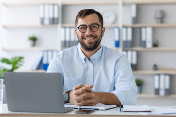Fototapeta premium Happy middle aged caucasian man with beard in glasses working with laptop in office or flat interior, free space. Business and work at home, freelance, webinar, remote meeting due covid-19 quarantine