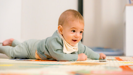 Happy baby crawling on colorful play mat indoors