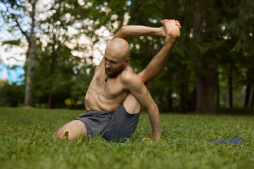 Unclothed individual practicing deep seated twist in open air