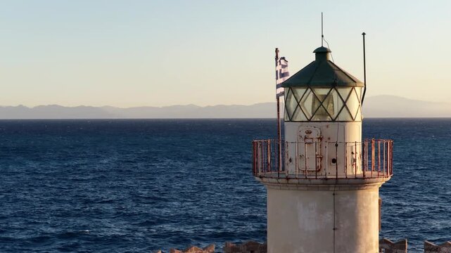 Rhodes lighthouse near saint nicholas fortress in early morning light showing greek flag