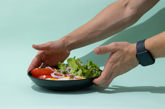 male hands placing a plate with fresh salad on a light green background healthy eating concept balanced nutrition natural food and healthy lifestyle