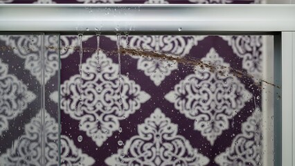 Leaking shower head with water droplets on purple and white tile background