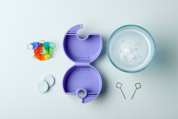Neat flat lay shows orthodontic retainer kit with purple case, cleanser bowl, tablets, and expansion keys on pale blue surface.
