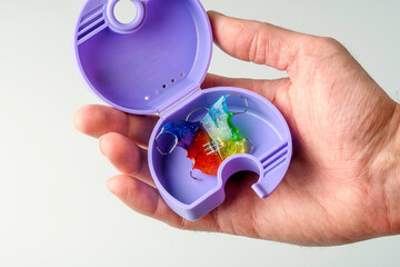 Adult hand presents open retainer case with colorful orthodontic appliance, simple routine for child dental alignment and hygiene.