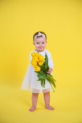 little girl in white dress on yellow background. Cheerful happy child with tulips flower bouquet