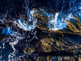Waves crash against rocky shore at high tide in a coastal area during the afternoon light providing a striking view of nature's energy and power