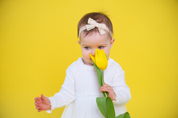 Cheerful happy child with tulip flower. little girl in white dress on yellow background. 