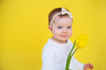 Cheerful happy child with tulip flower. little girl in white dress on yellow background. 