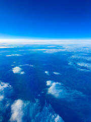 View of the sky with clouds and distant land captured from an airplane at high altitude during daytime with bright blue skies