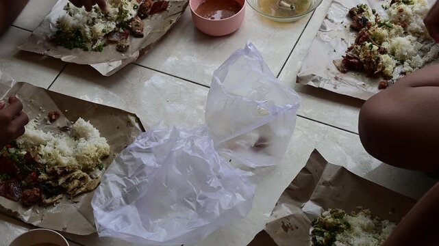 Authentic Balinese Nasi Campur Babi served in paper wrap on floor during traditional group meal in Indonesia