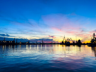 Sunset at the harbor with cranes and calm water reflecting colors in the sky during evening hours